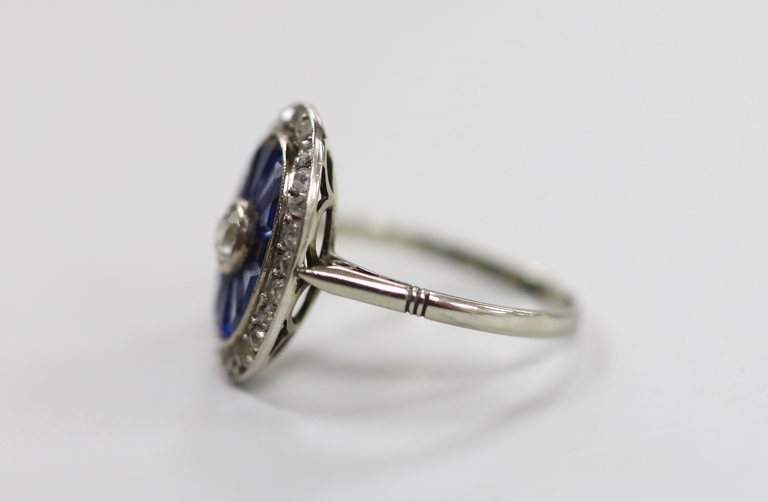 A 1920's white metal, sapphire and diamond oval cluster ring, set with round cut diamonds and shaped cut sapphires, size M/N, gross weight 3.3 grams.